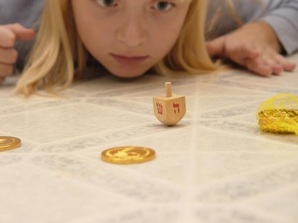 young blo<em></em>nde girl playing dreidel with gelt on table